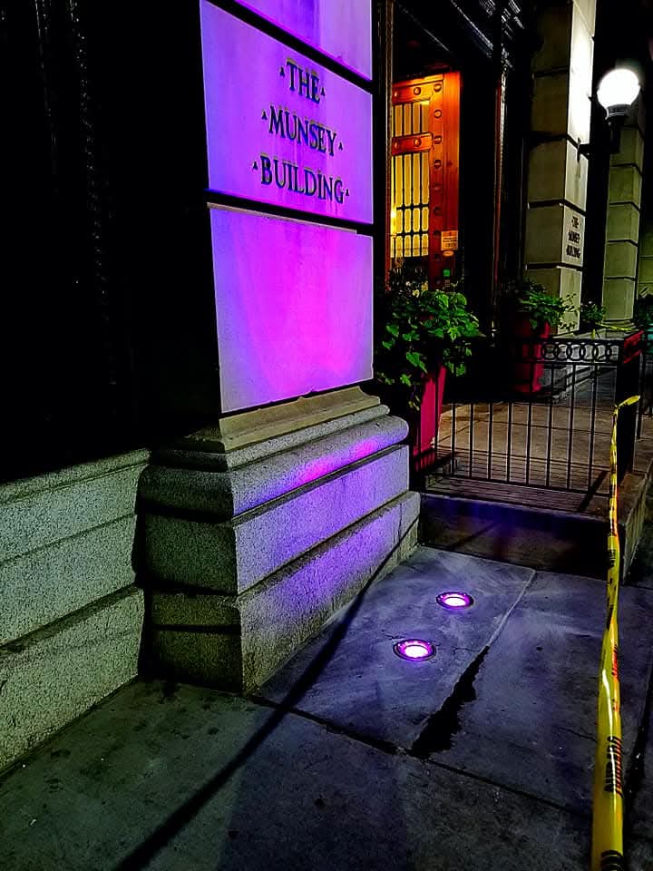 Building entrance with in-ground uplights washing the stone facade in purple light