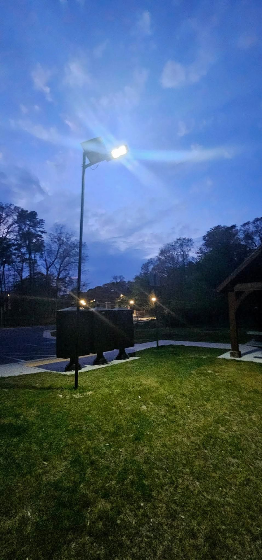 Solar LED pole light lighting a pavilion and parking area at dusk