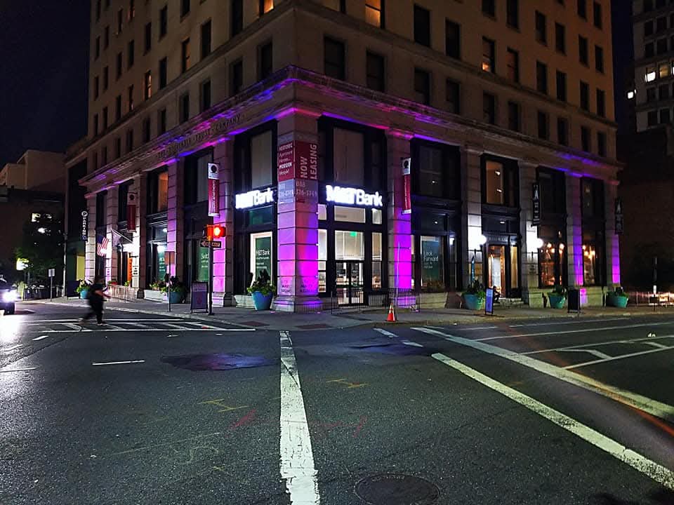 Historic corner office building lit at night with purple and blue architectural uplighting