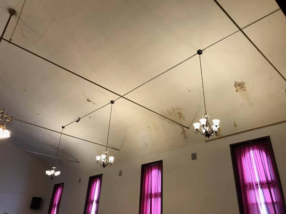 Hall ceiling with hanging chandeliers on conduit runs above tall curtained windows