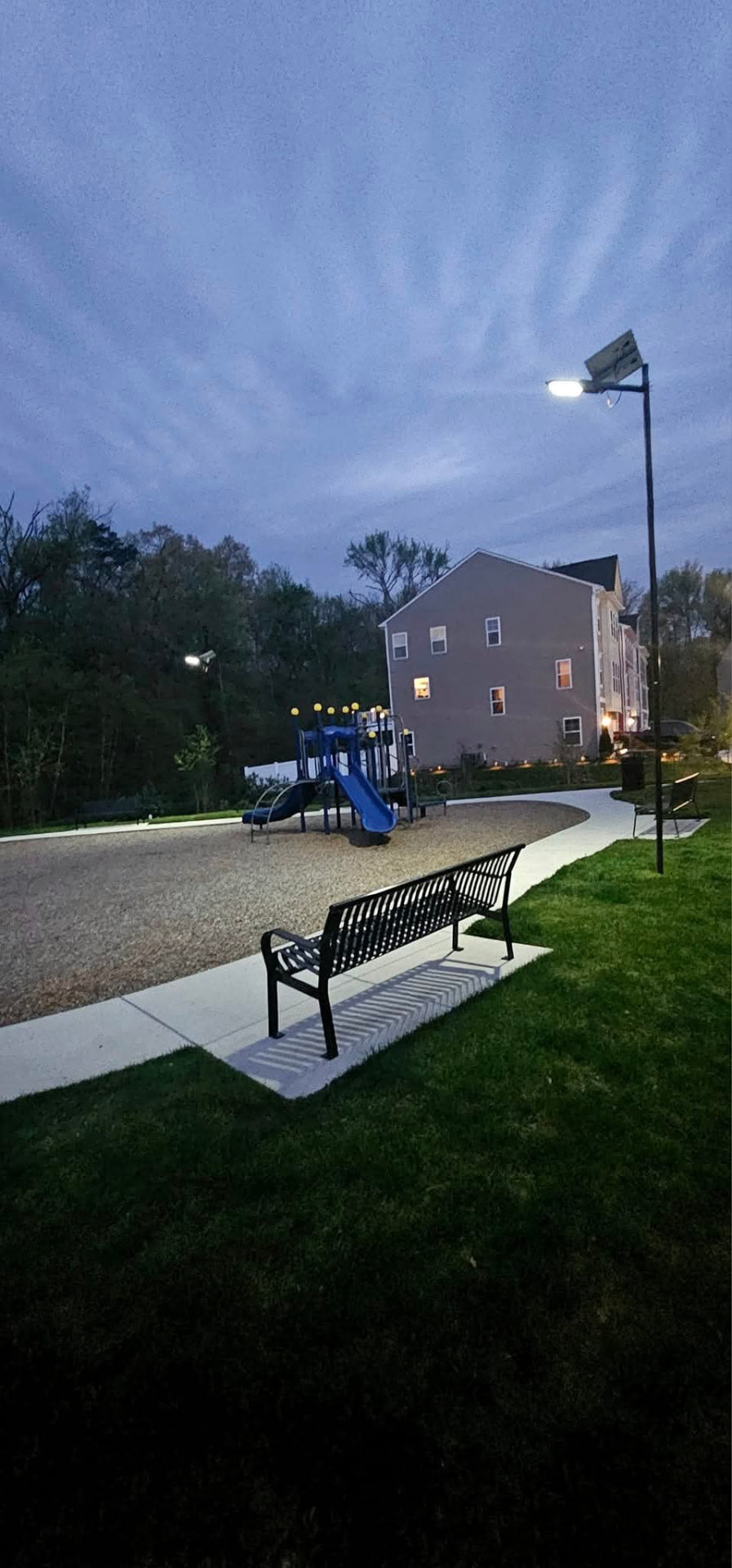 Community playground and walkway lit by a solar LED pole light at night