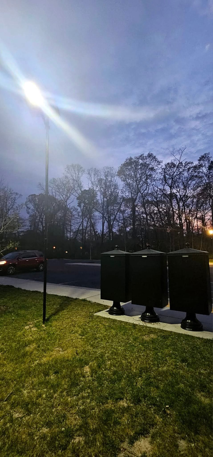 Solar LED pole light illuminating a parking lot and walkway at dusk