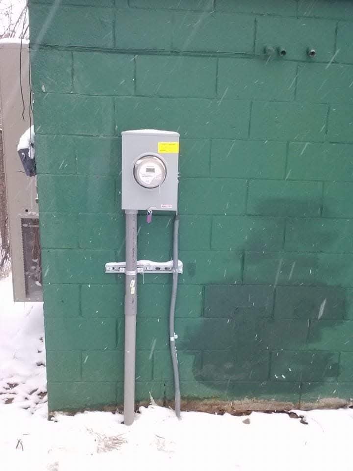 New exterior electric meter and service riser installed on a block wall in the snow