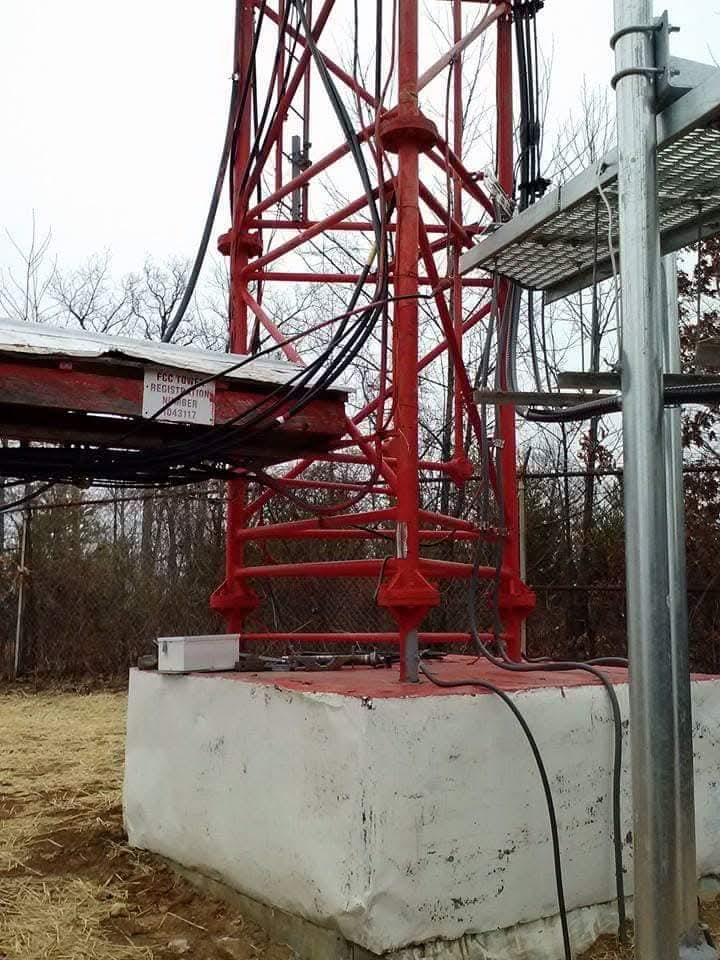 Communications tower base with power feed and grounding conductors